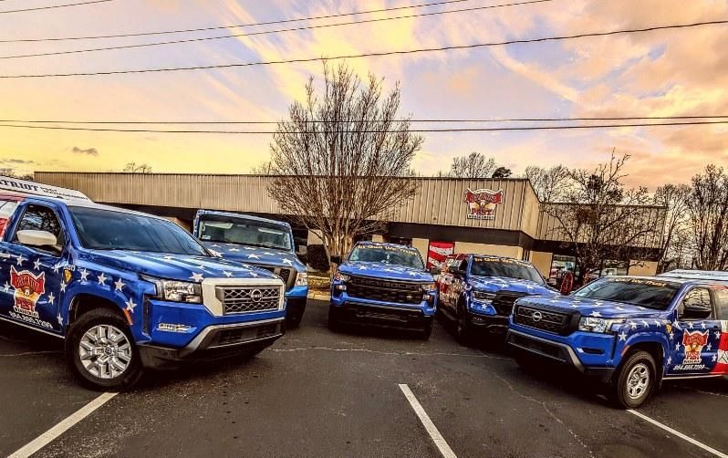 Blue company trucks parked outside a building with an American flag theme at sunset.