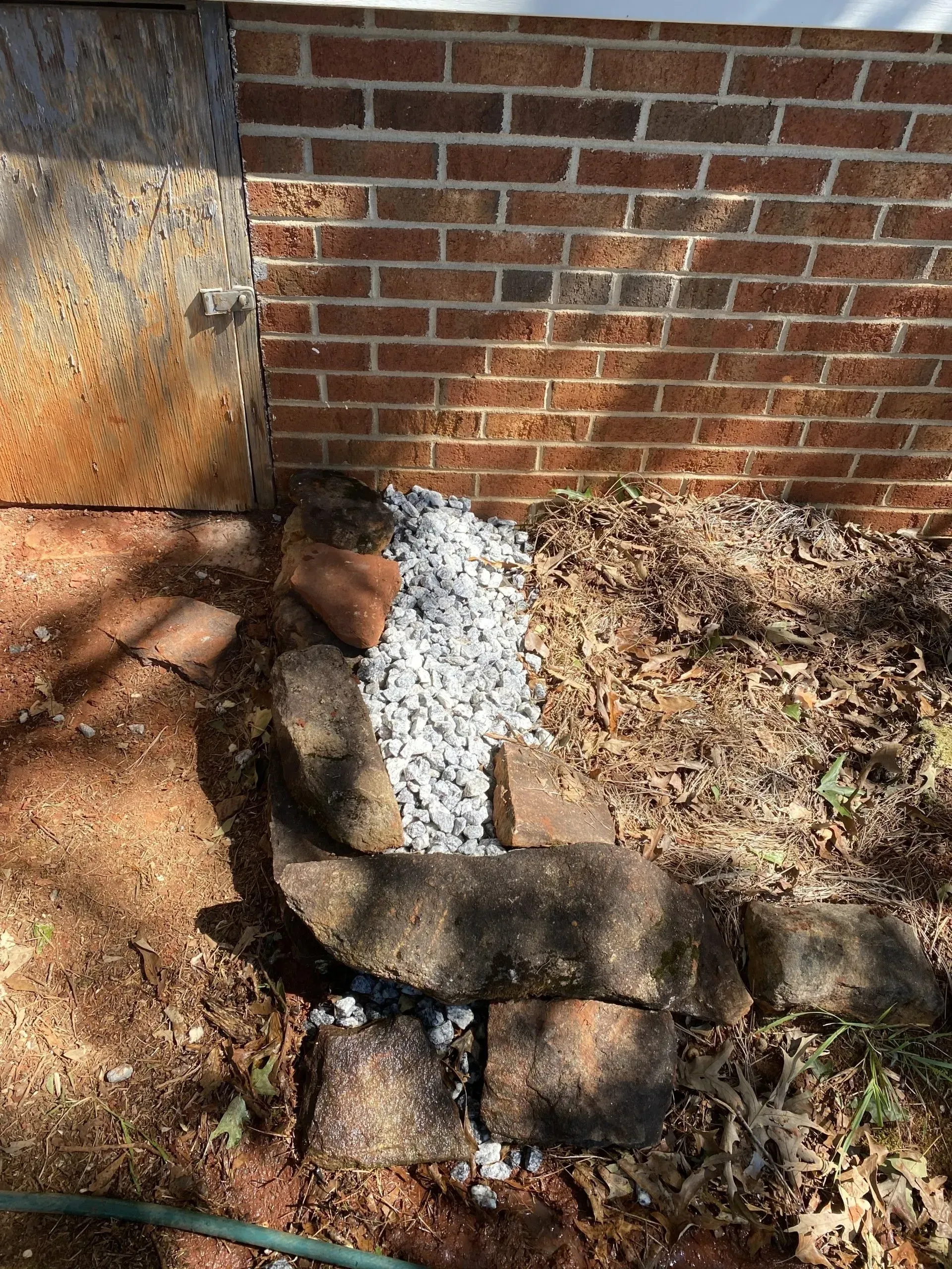 Brick wall and foundation with stones and gravel at the base, surrounded by dirt and debris.