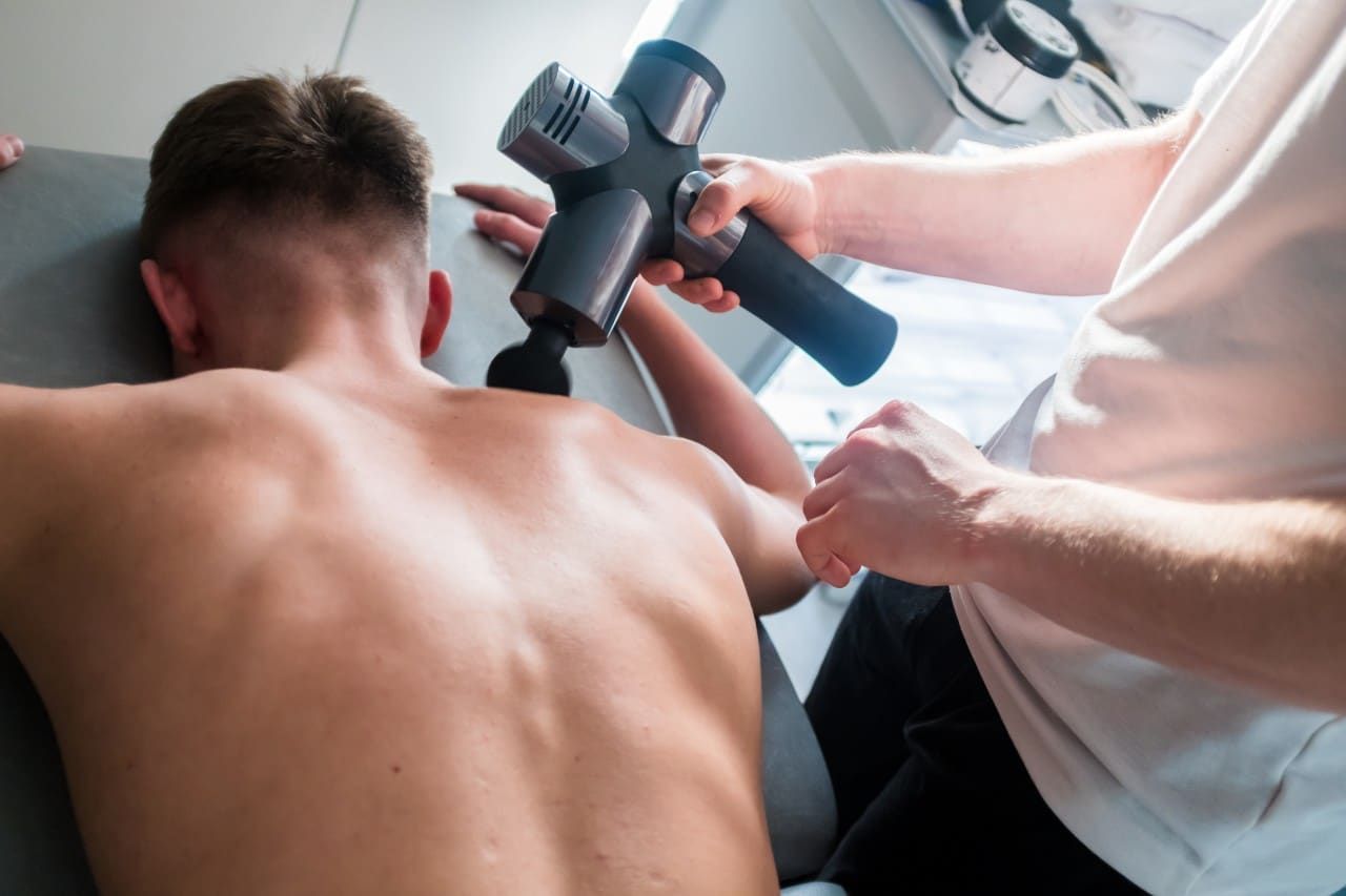 Person receiving a back massage with a handheld percussion massager on a treatment table