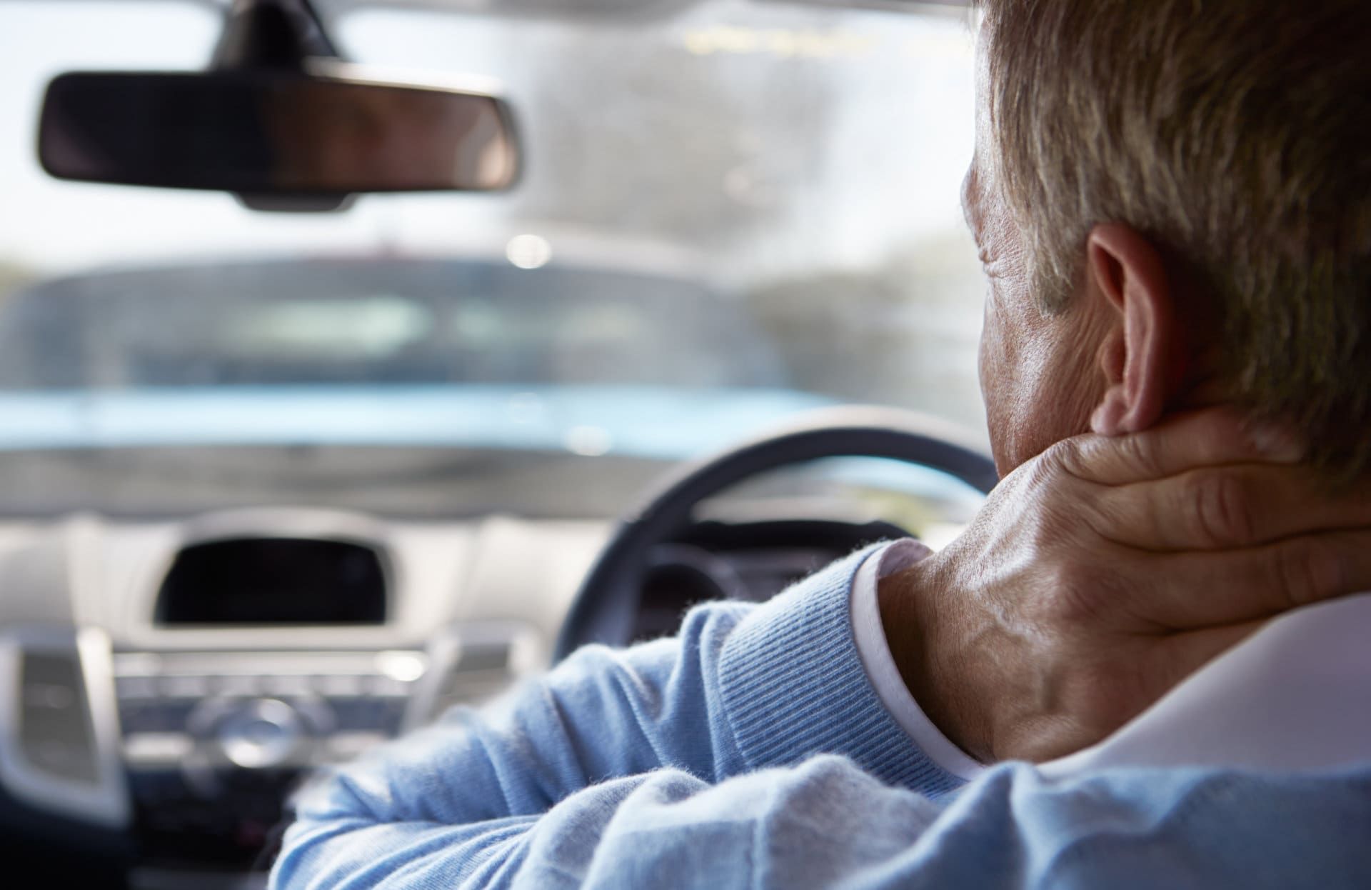 Person in a car rubbing the back of their neck while driving, seen from the back seat