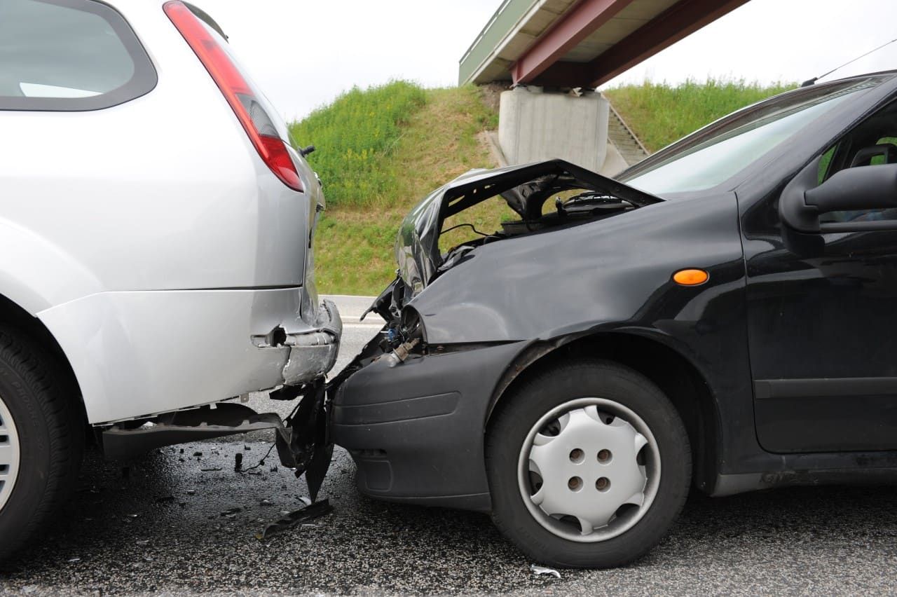 Black car rear-ends silver car under an overpass, showing collision damage.