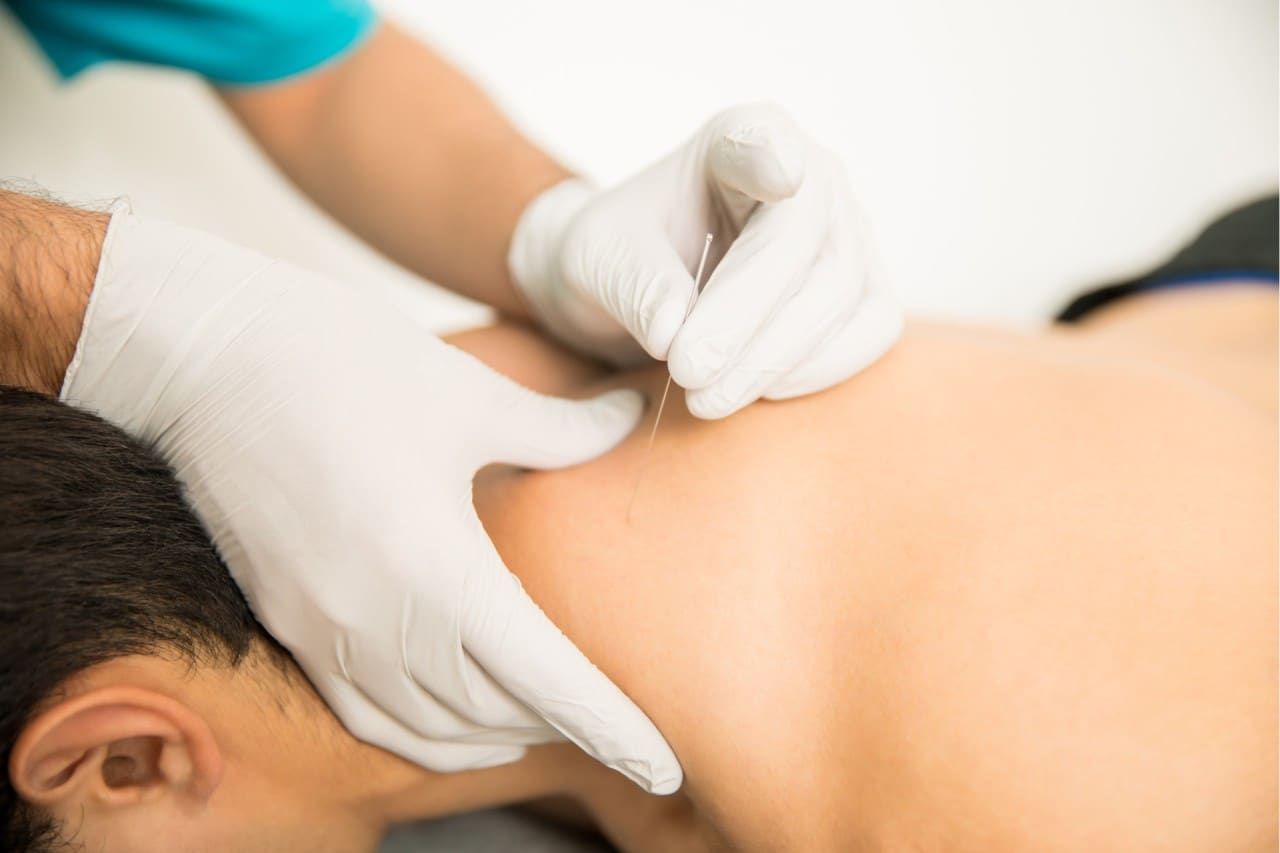 Gloved hands performing a shoulder massage on a person lying face down