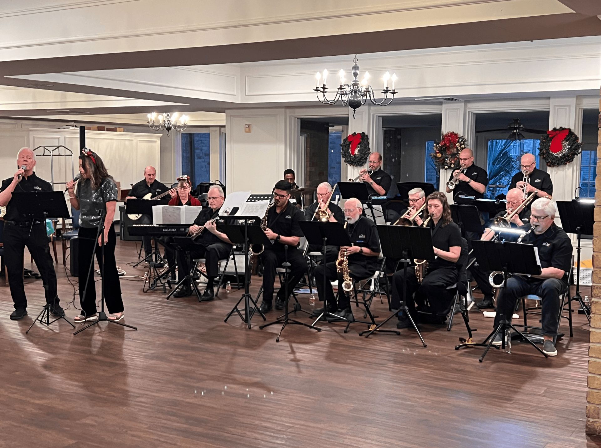 A live band performing in a decorated room. Musicians play instruments, with two vocalists at the front.