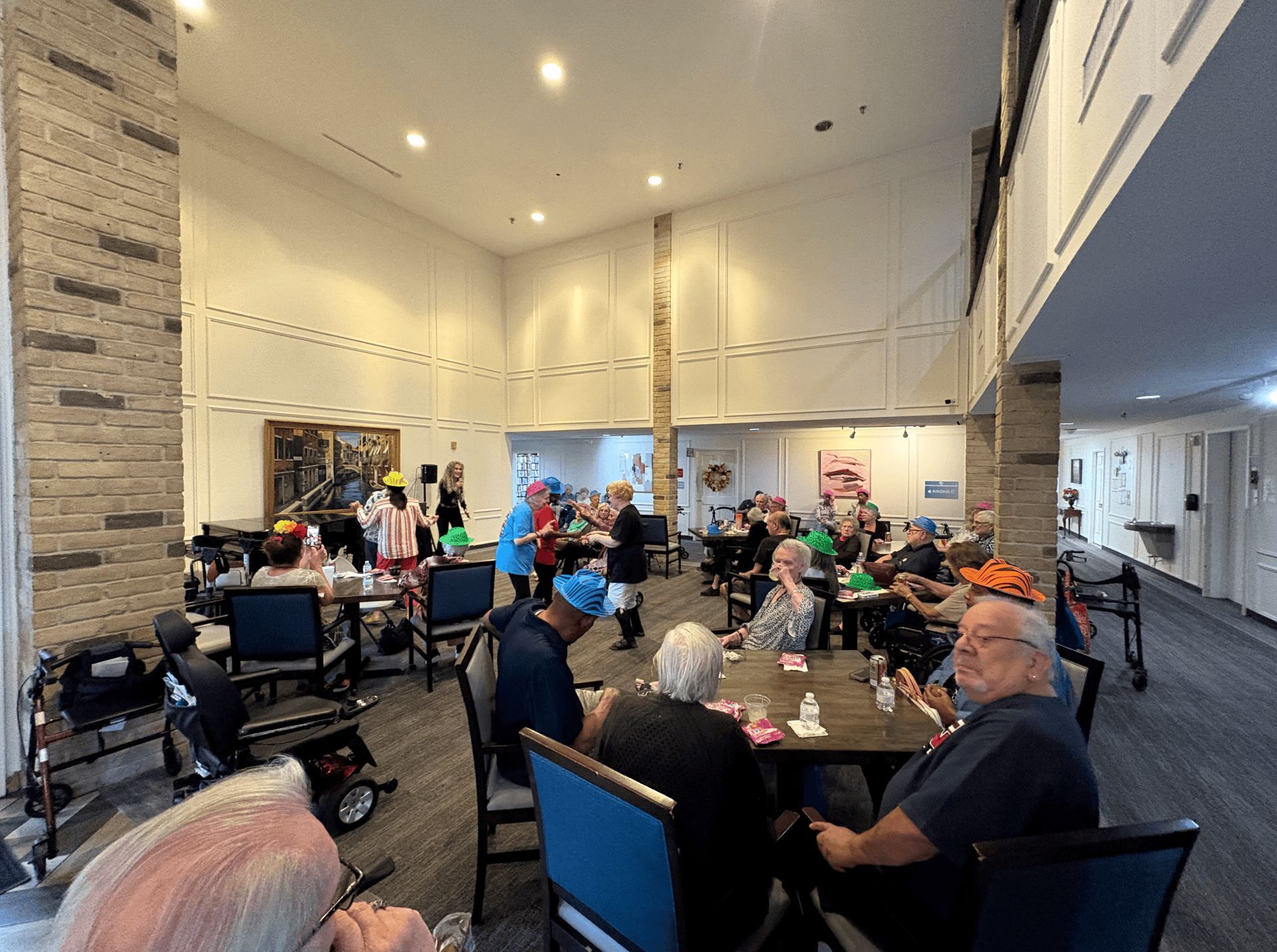 Seniors play games in a community room with high ceilings. Some wear silly hats.