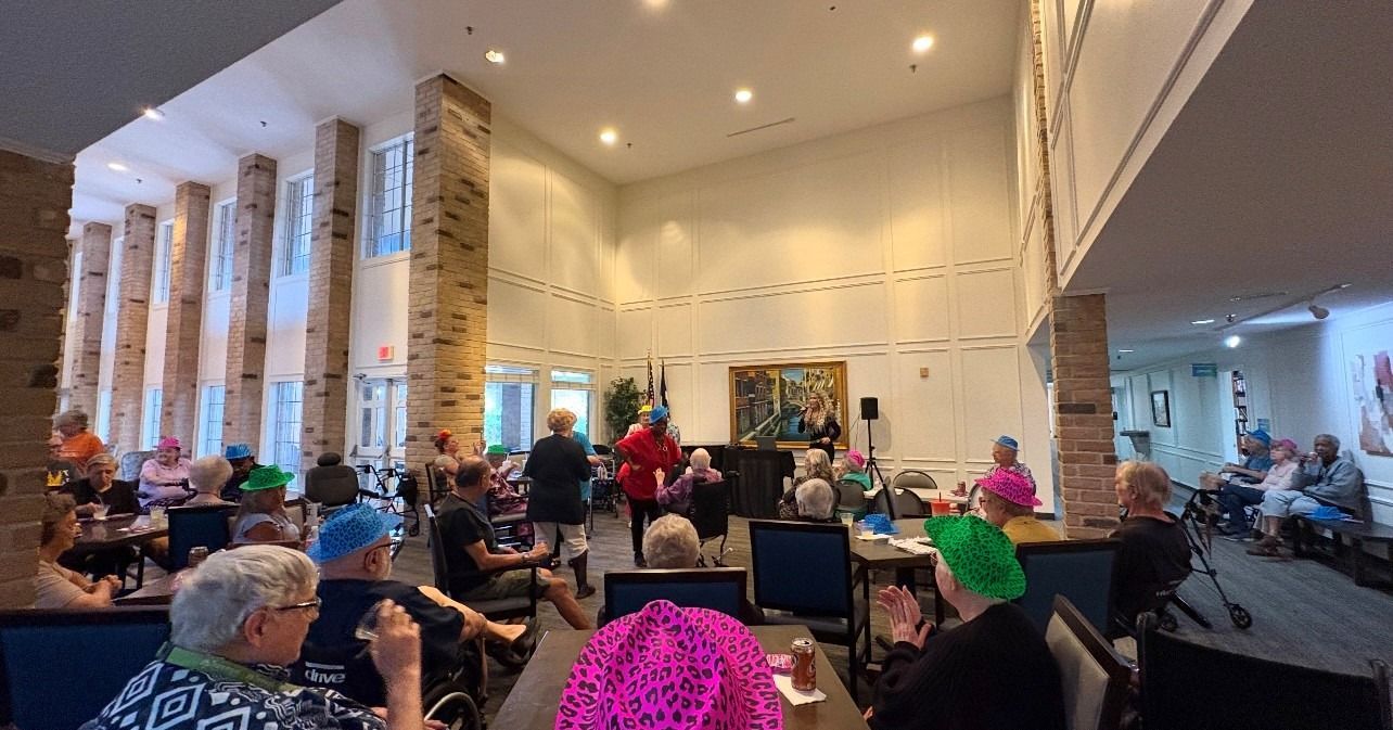 People in colorful wigs watch a presentation in a large room.