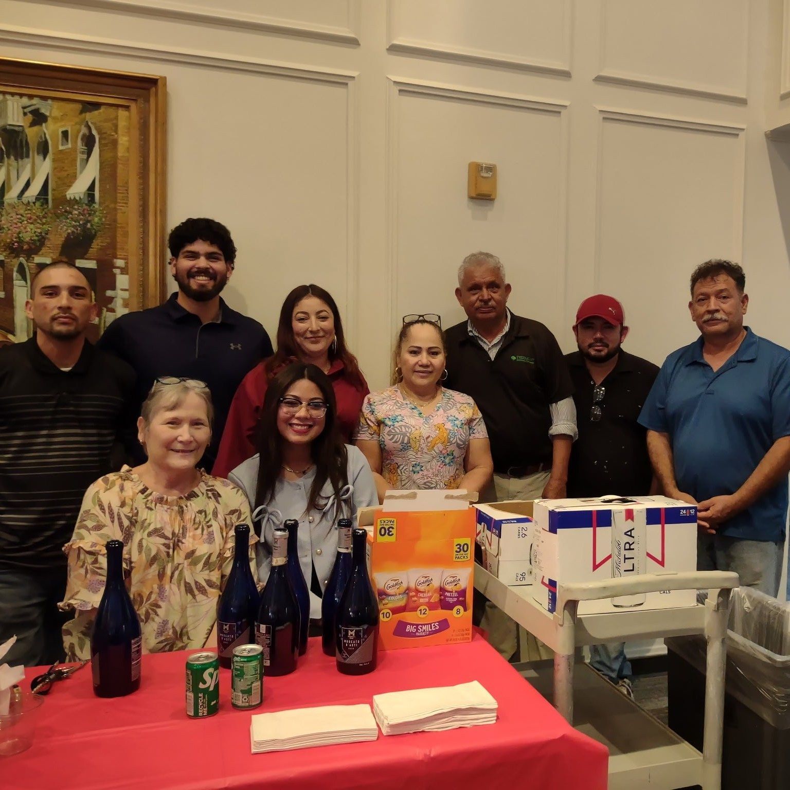 Group of people behind a table with drinks and boxes, likely preparing for an event indoors.