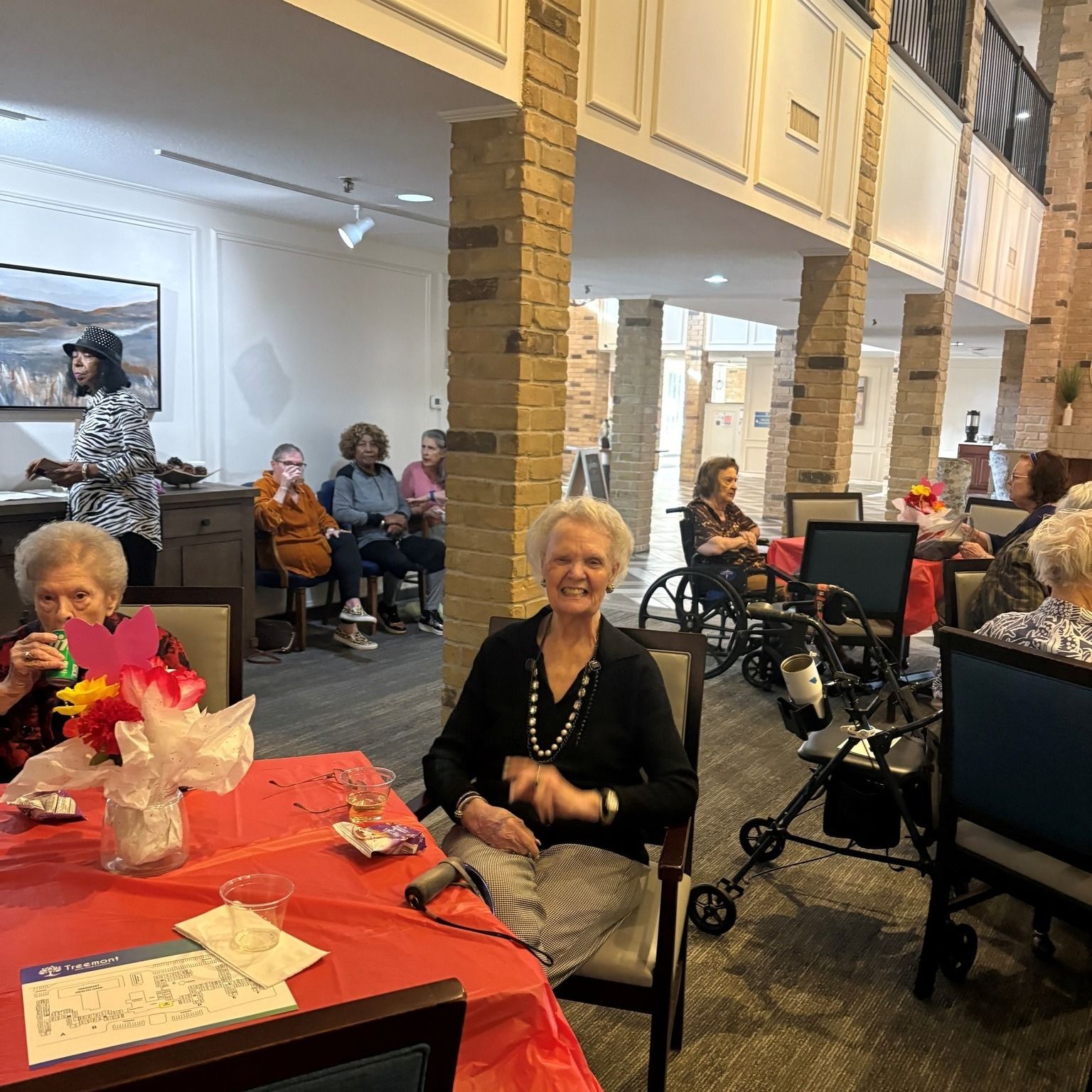 Seniors seated at tables and in chairs, enjoying a social gathering in a well-lit interior.