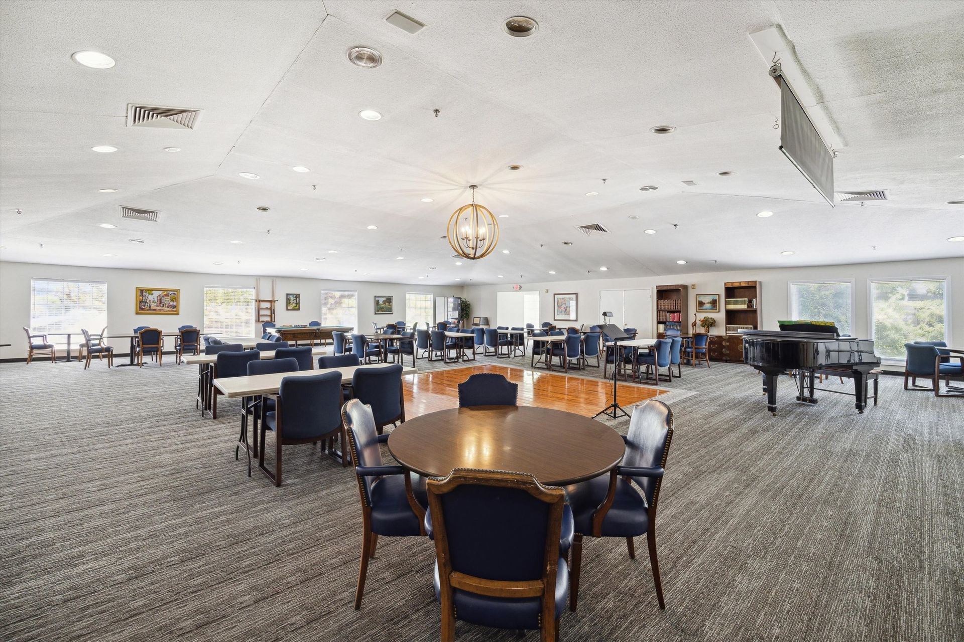 Large, open room with round and rectangular tables, seating, and two pianos, under a high ceiling.