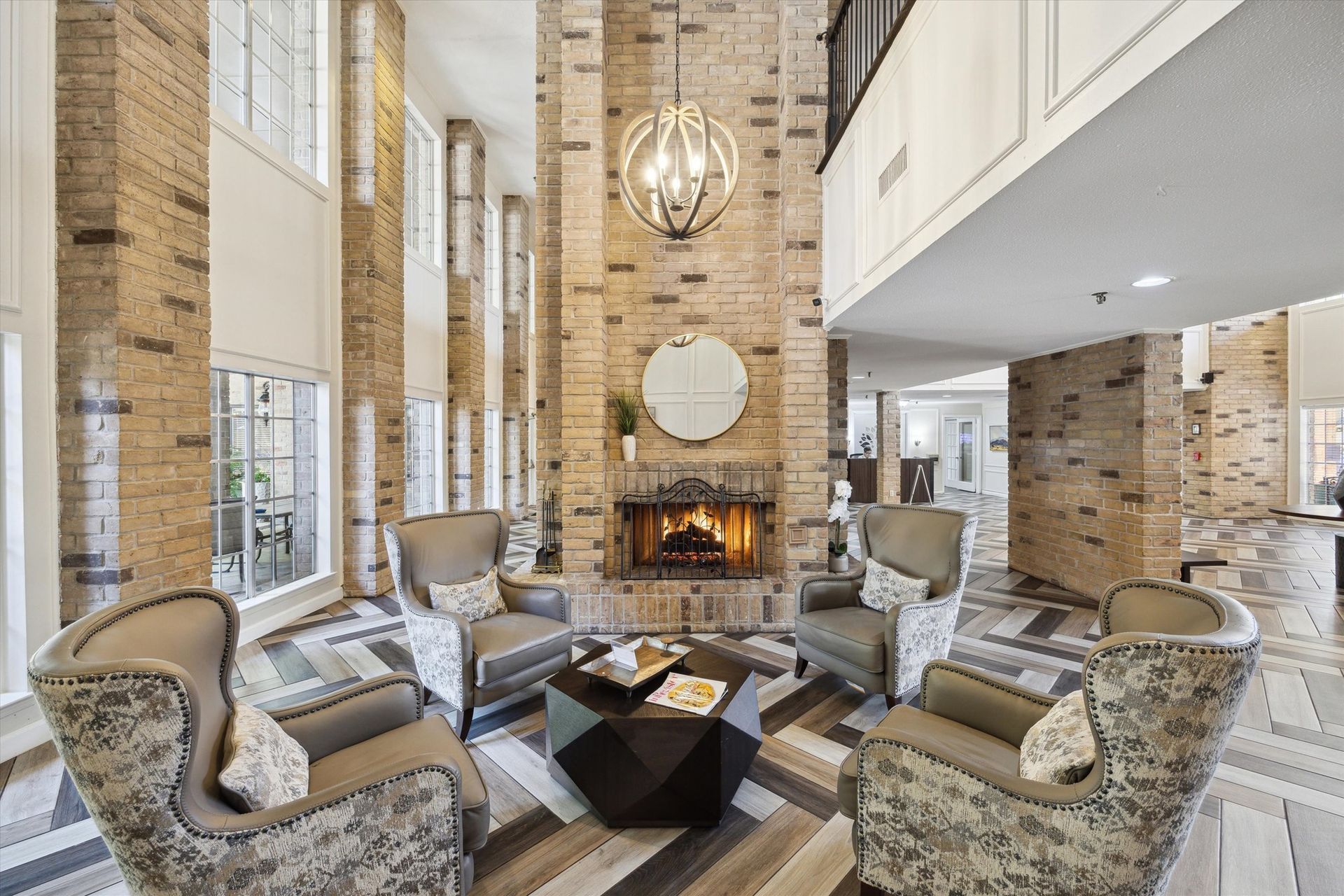 Cozy lobby with a brick fireplace, armchairs, geometric coffee table, and large windows.