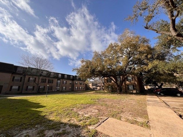 Apartment building with a large tree in front under a partly cloudy blue sky.