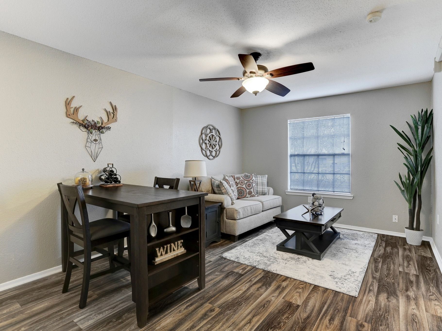 Living room with dark wood table and chairs, couch, and faux plants.