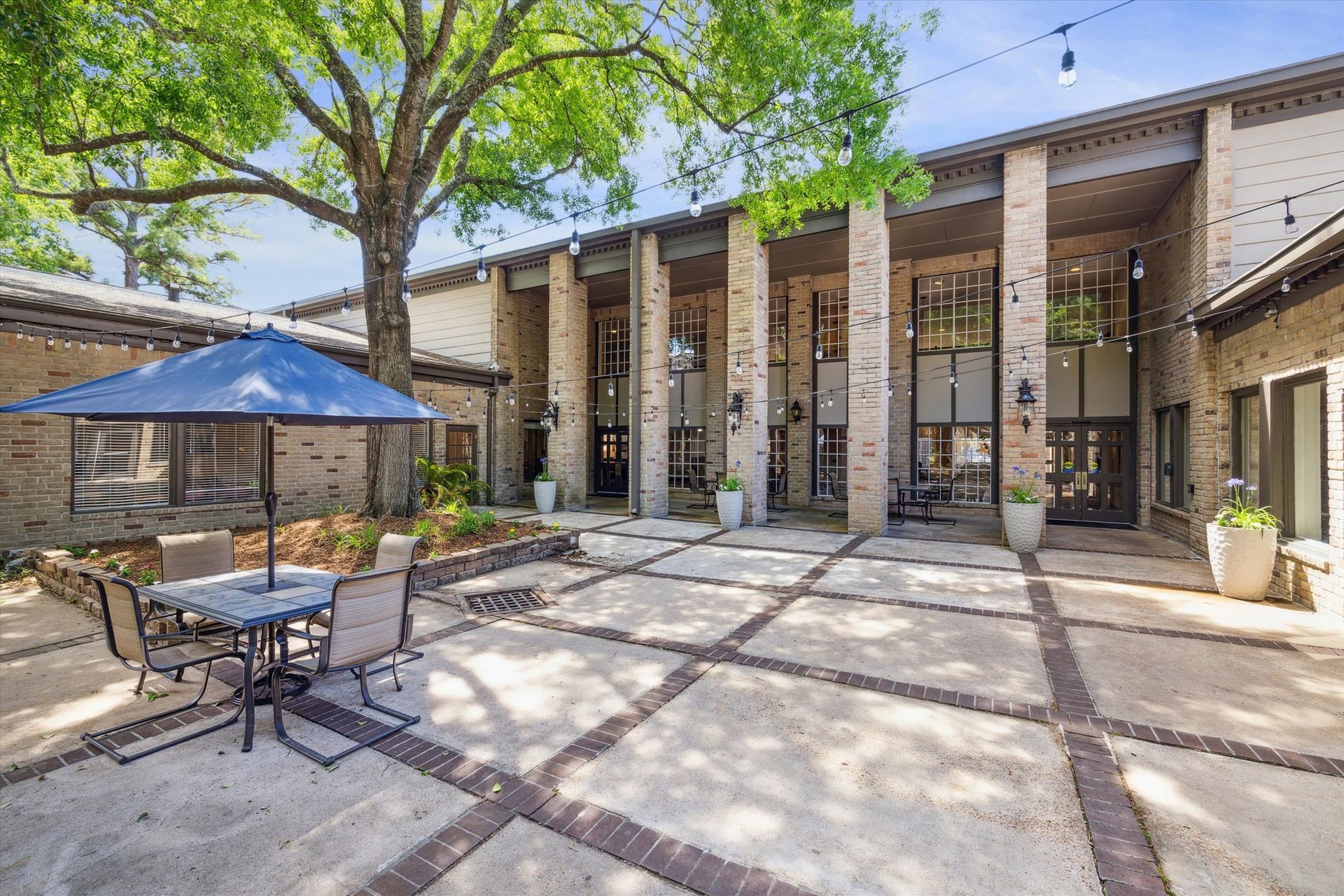 Patio with seating area and large brick building with decorative columns. Blue umbrella.