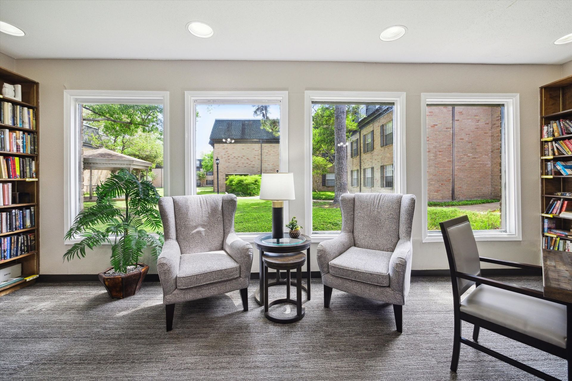 Reading room with two patterned armchairs, small table, and windows overlooking a garden. Bookshelves on either side.