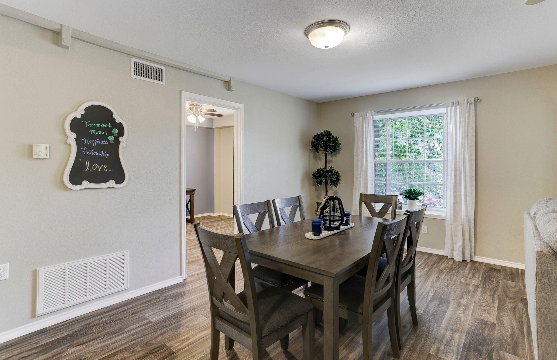 Dining room with a table and six chairs, window, chalkboard, wood-look floors, and neutral-colored walls.