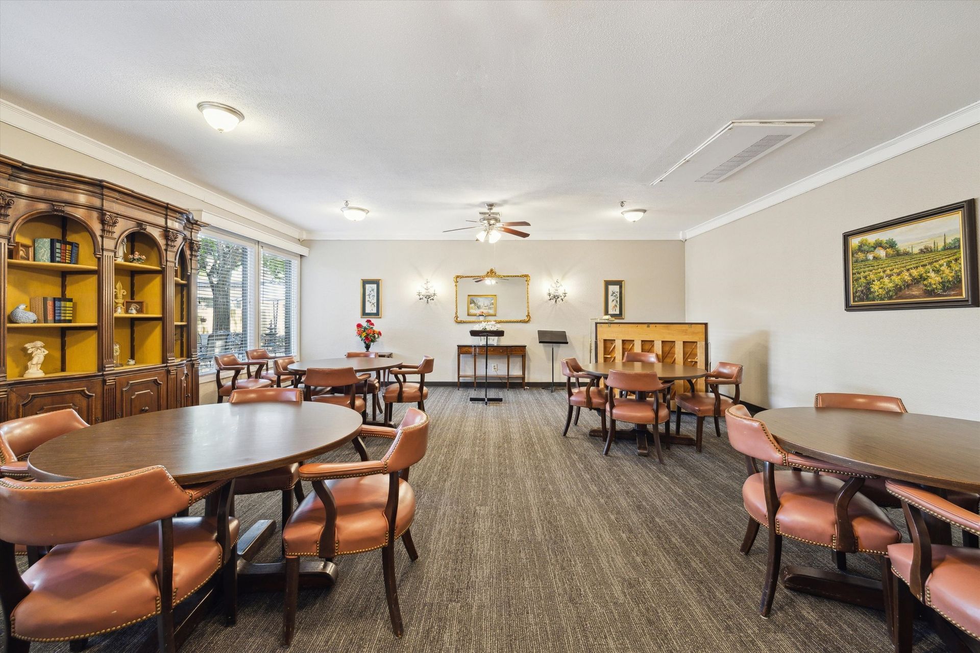 A well-lit community room with round tables, chairs, bookshelves, and a music stand.