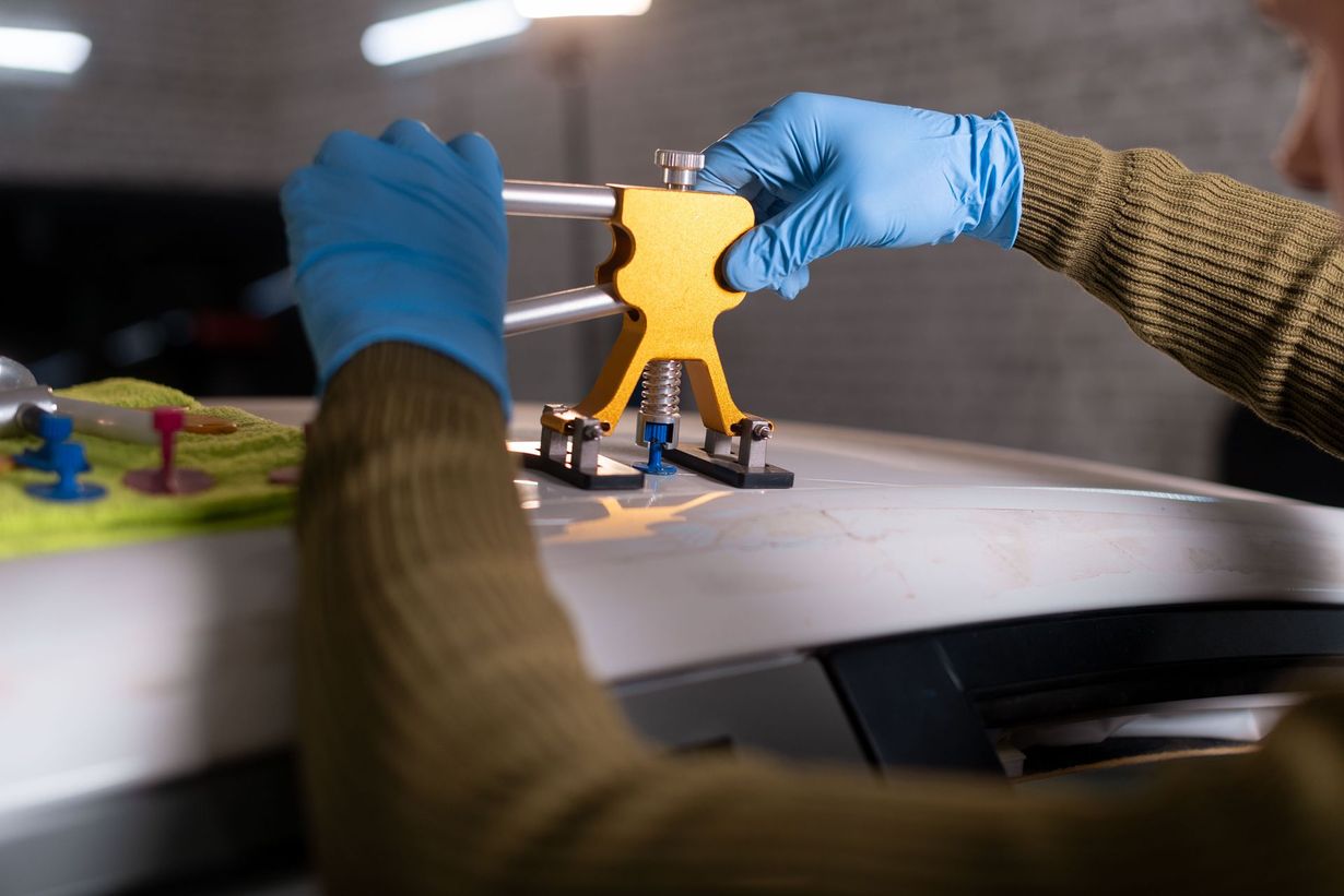Person using dent repair tool on a white car, wearing blue gloves.