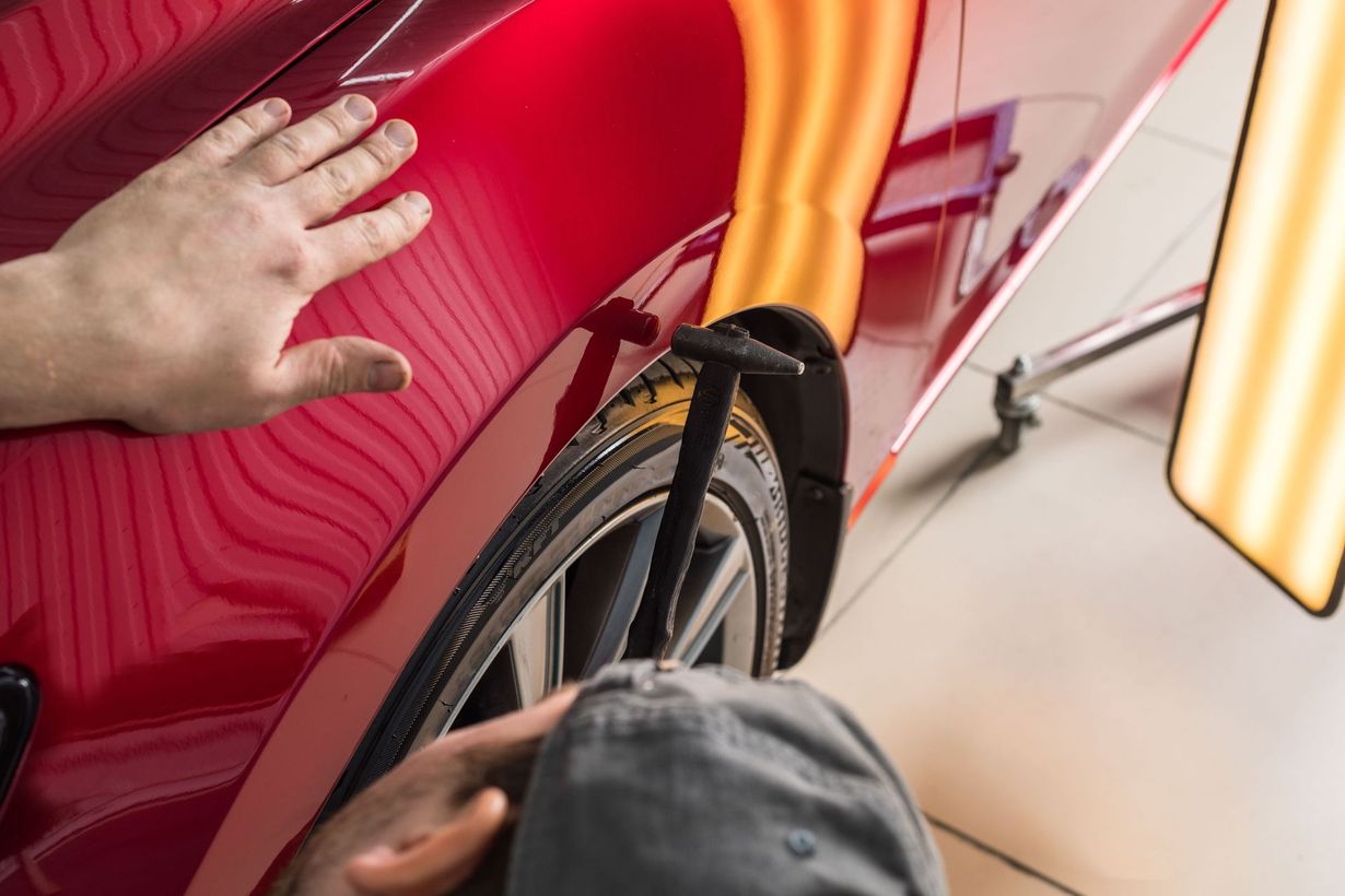 Person applying ceramic coating to a red car's taillight with a gloved hand in a shop.