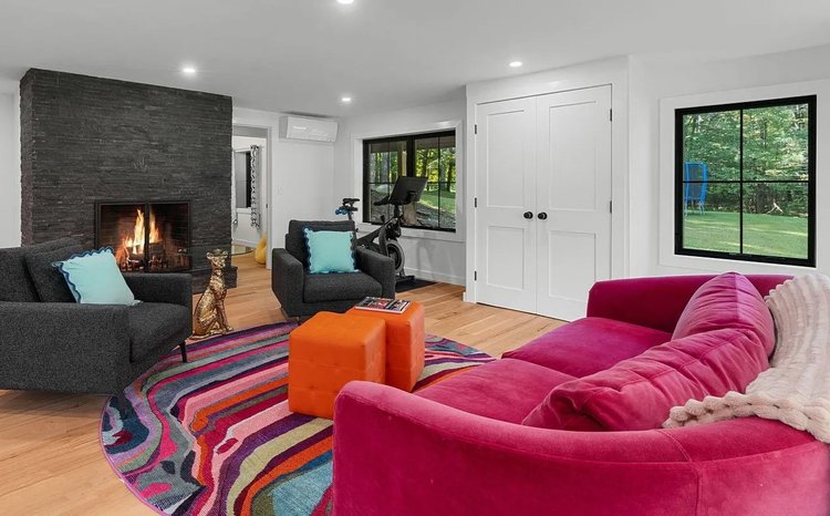 A living room with a pink couch , chairs , and a fireplace.