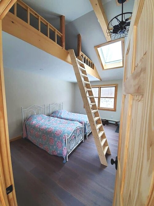 A bedroom with two beds and a staircase leading to a loft.