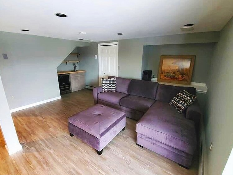 A living room with a purple sectional couch and ottoman.