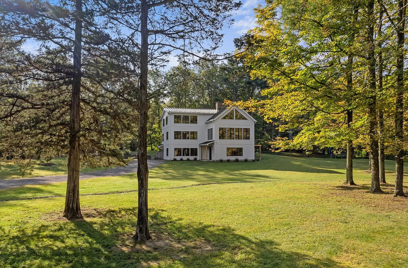 A large white house is sitting in the middle of a lush green field surrounded by trees.