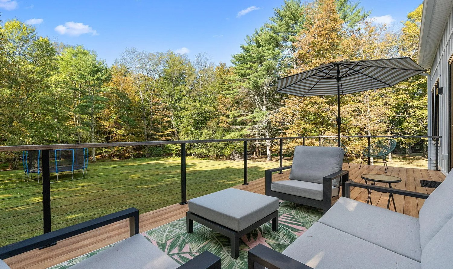 A deck with a couch , chair , ottoman and umbrella.