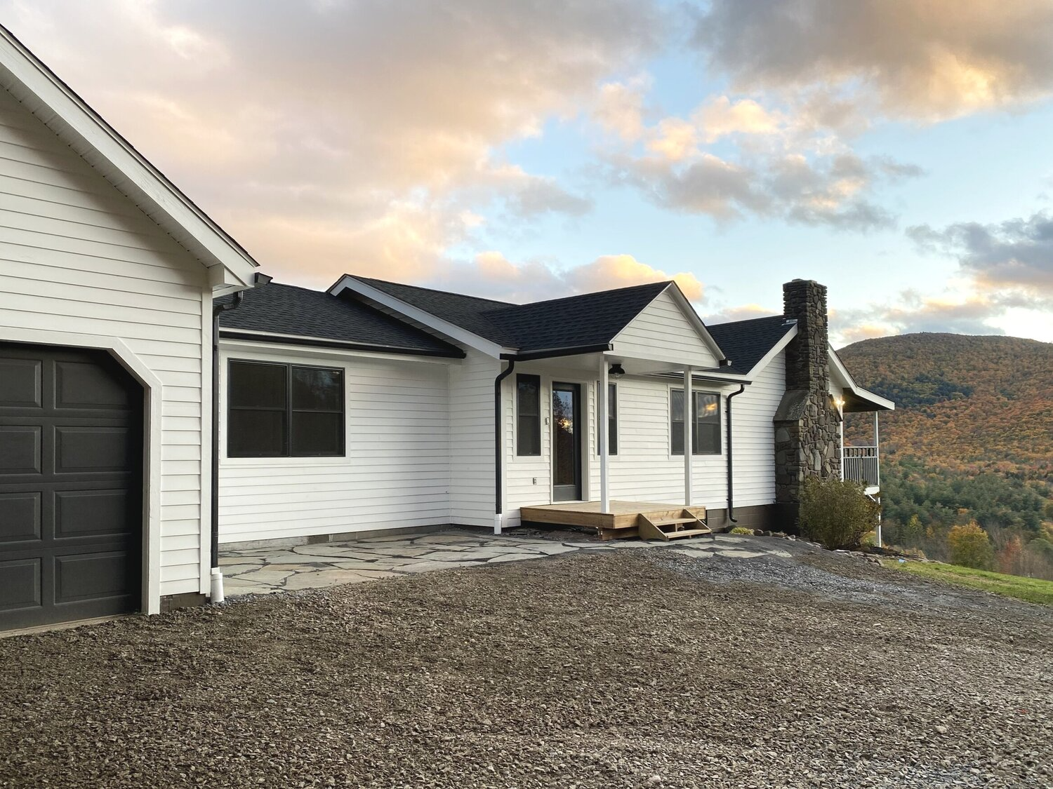 A white house with a black garage door is sitting on top of a gravel hill.