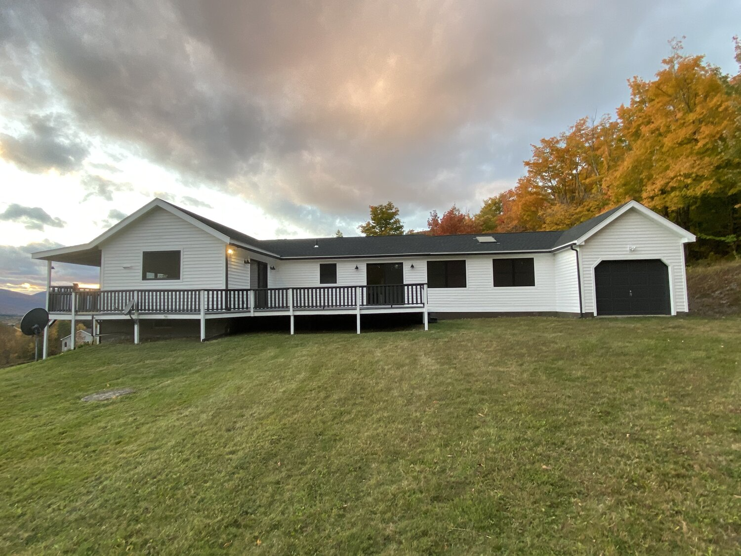 A white house with a black garage is sitting on top of a lush green hillside.