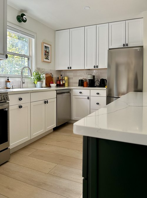 A kitchen with white cabinets , stainless steel appliances , and a green island.