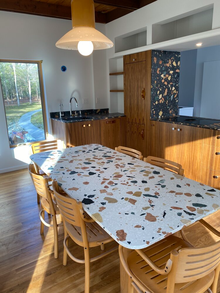 A dining room with a table and chairs and a kitchen in the background.