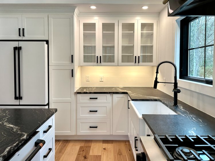 A kitchen with white cabinets , black counter tops , a sink and a refrigerator.