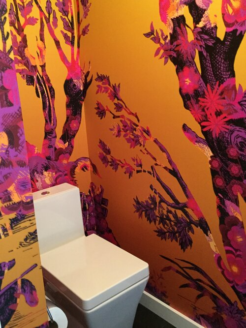 A toilet in a bathroom with a mural on the wall