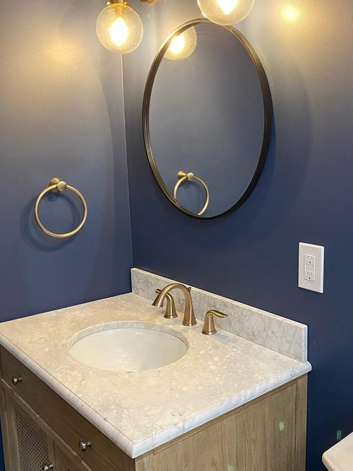 A bathroom with a sink , mirror and towel rings.