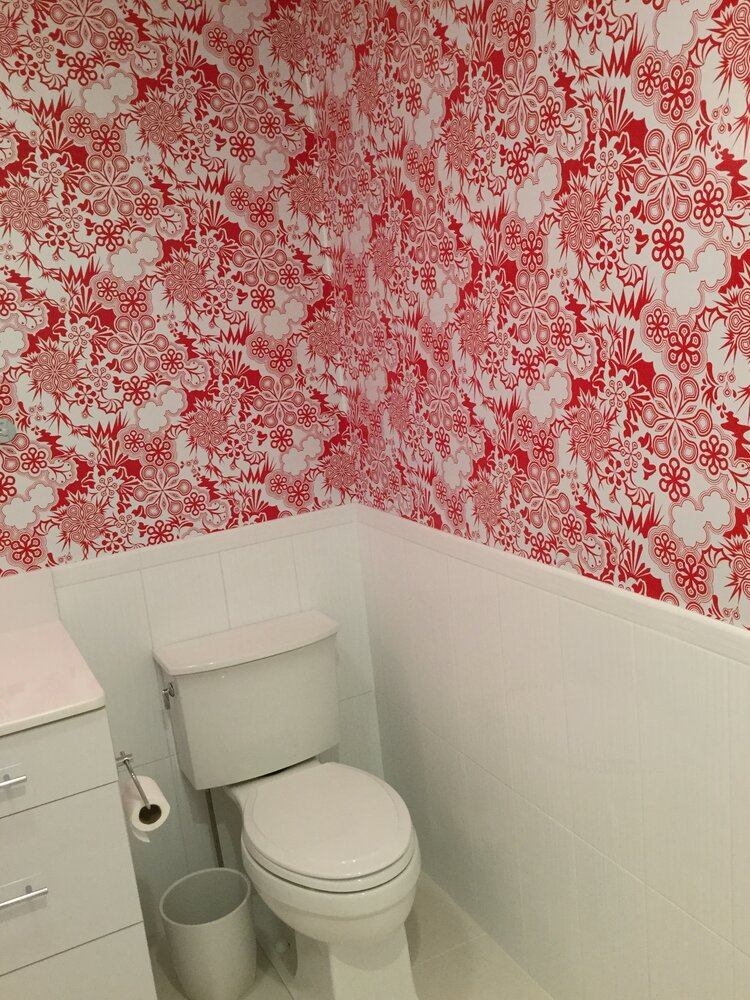 A bathroom with a toilet , sink , and red and white wallpaper