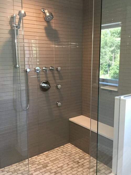 A walk in shower with a glass door and a bench.