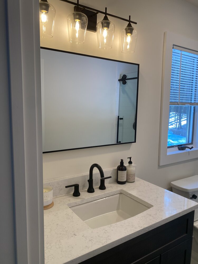 A bathroom with a sink , mirror and window.