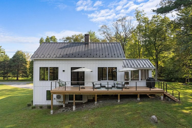 A white house with a black roof and a large deck.