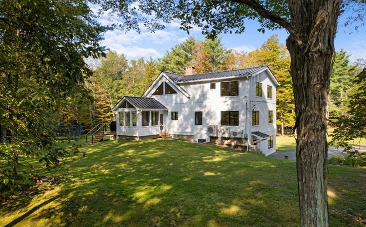 A large white house is sitting on top of a lush green hill surrounded by trees.
