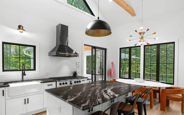 A kitchen with a large island , stove , sink , chairs and a table.