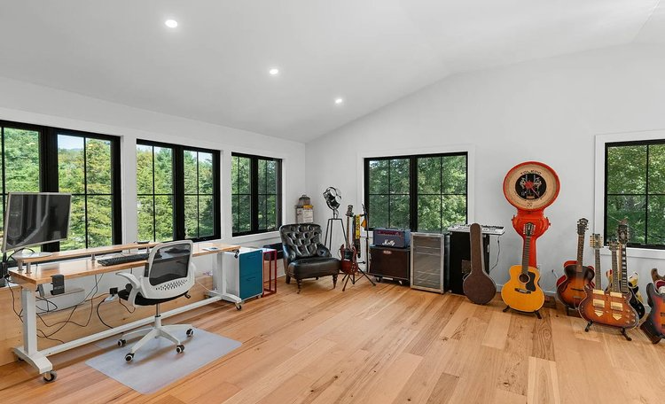 A room with a lot of guitars on the floor and a desk.