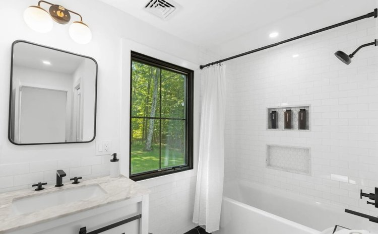 A bathroom with a sink , tub , mirror and window.