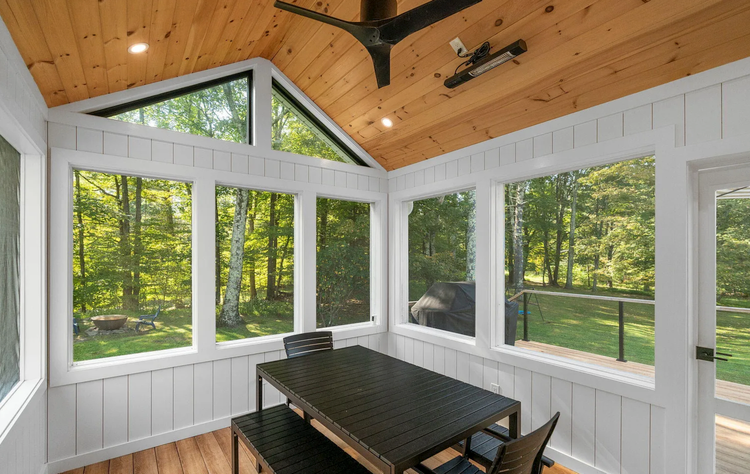 A screened in porch with a table and chairs and a ceiling fan.