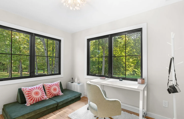 A room with a couch , desk , chair and two windows.