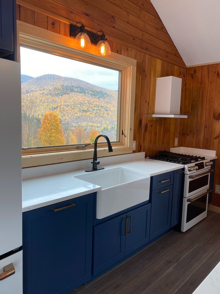A kitchen with blue cabinets , a sink , a stove , and a window.