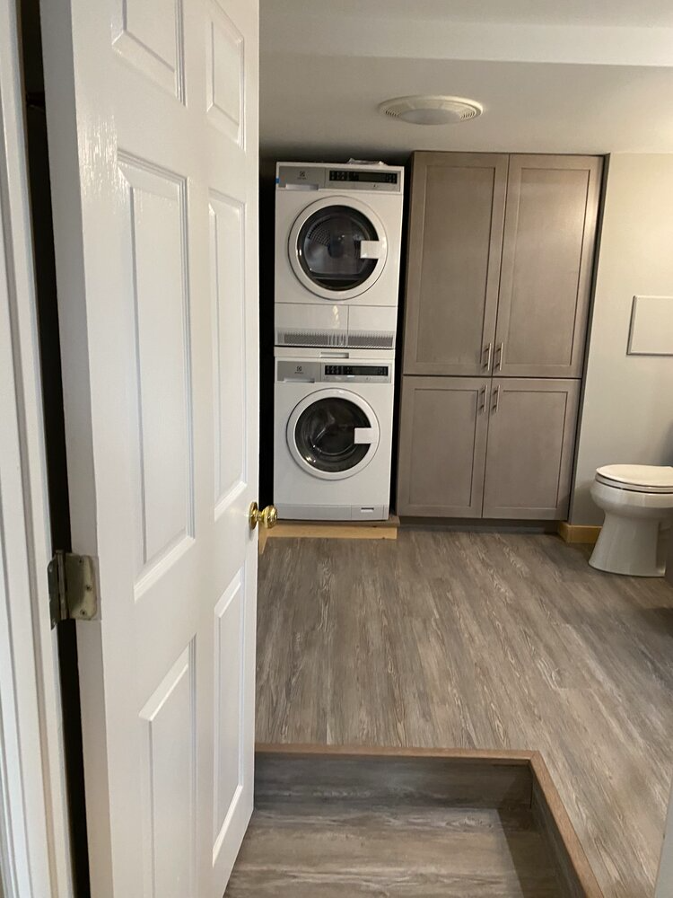 A laundry room with a washer and dryer stacked on top of each other and a toilet.