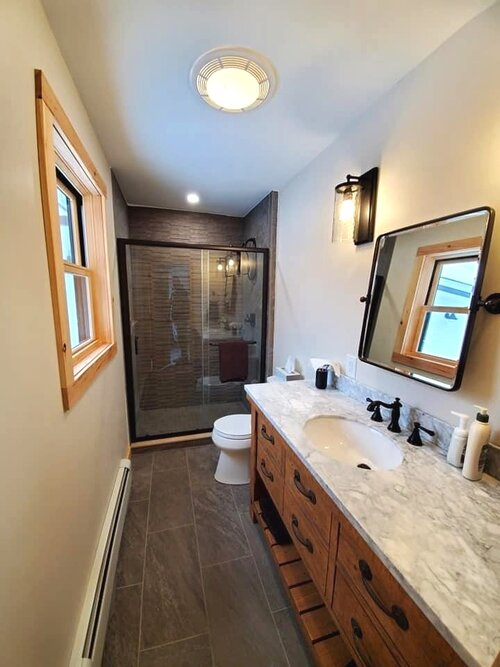 A bathroom with a toilet , sink , mirror and shower.