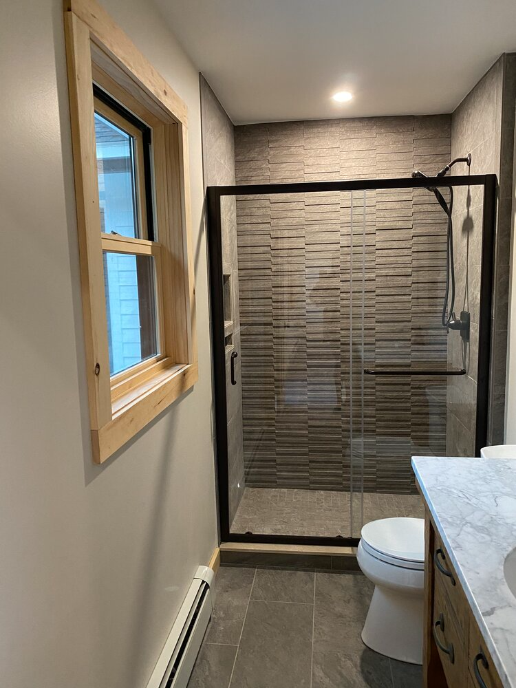 A bathroom with a toilet , sink , shower and window.