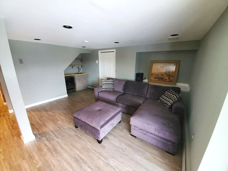 A living room with a purple sectional couch and ottoman.