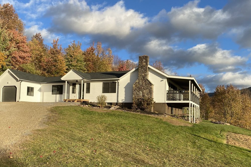 A white house is sitting on top of a grassy hill surrounded by trees.