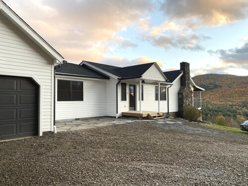 A white house with a black garage door is sitting on top of a hill.